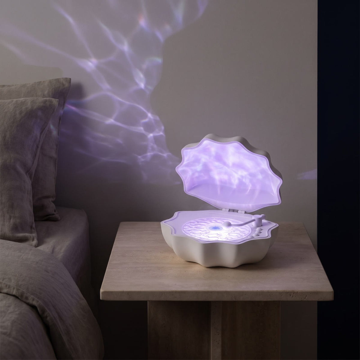 Lampka Lumina Muszelka biała włączona wieczorem na kamiennej szafce nocnej, liliowe fale światła na ścianie
